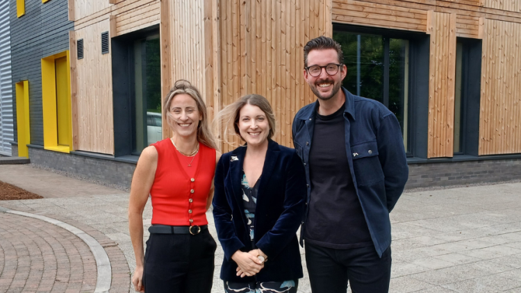 Three people stand smiling outside an industrial unit with a timber facade.
